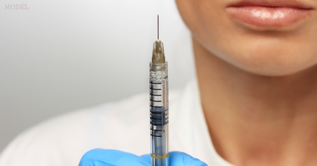 Female injector holding syringe and needle in gloved hand (model)