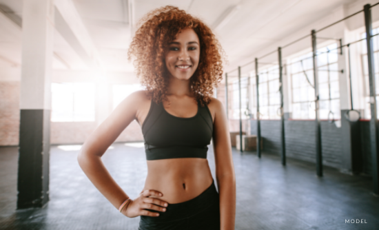 Fit woman in gym grins while flexing her arm muscles.