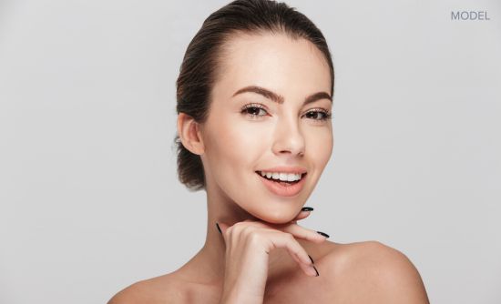 Woman with clear skin, holding her face in her hand (MODEL).